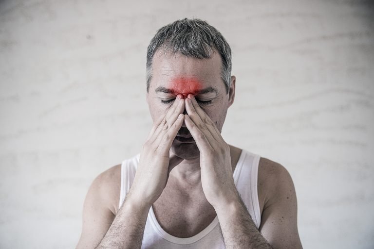 The man holds his nose and sinus area with fingers in obvious pa